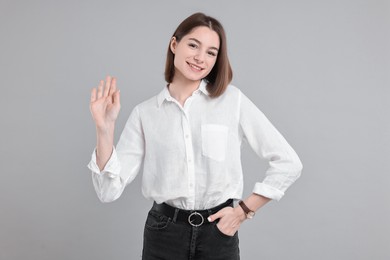 Happy teenage girl waving on gray background