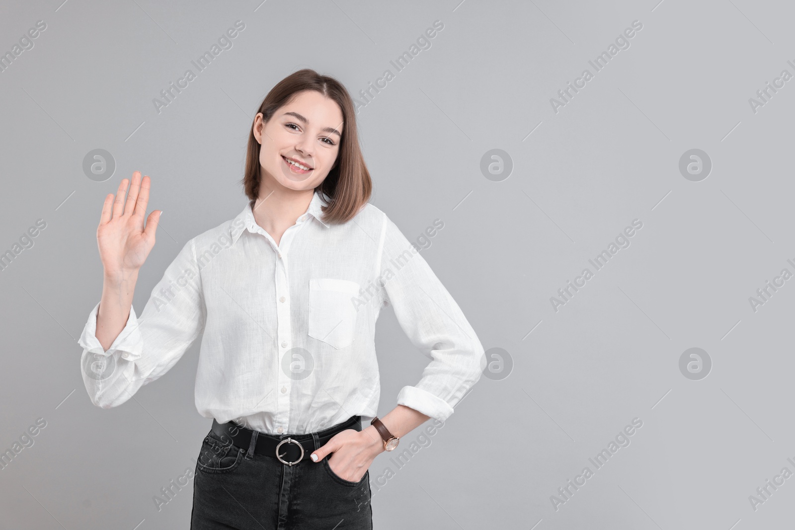 Photo of Happy teenage girl waving on gray background, space for text