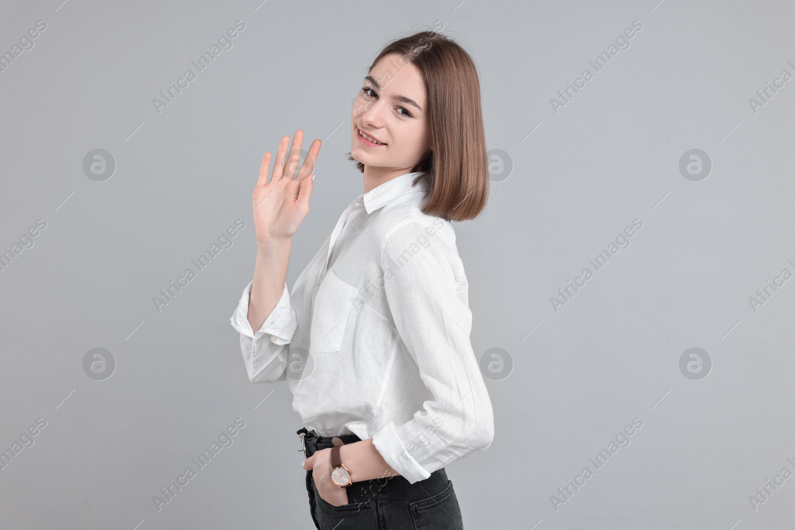 Photo of Happy teenage girl waving on gray background