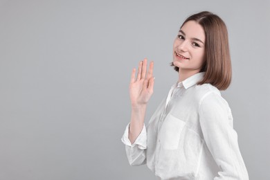 Happy teenage girl waving on gray background, space for text