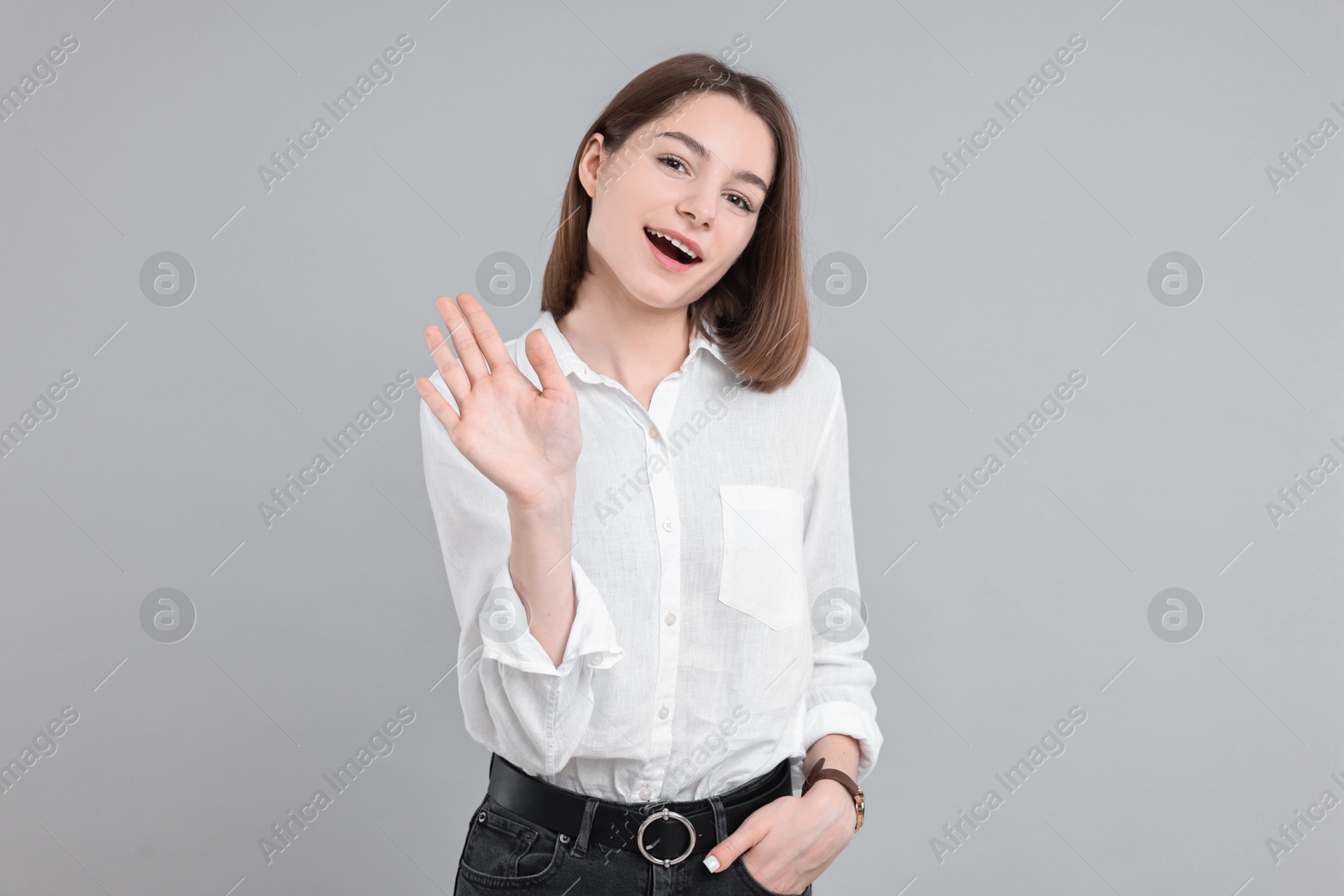 Photo of Happy teenage girl waving on gray background