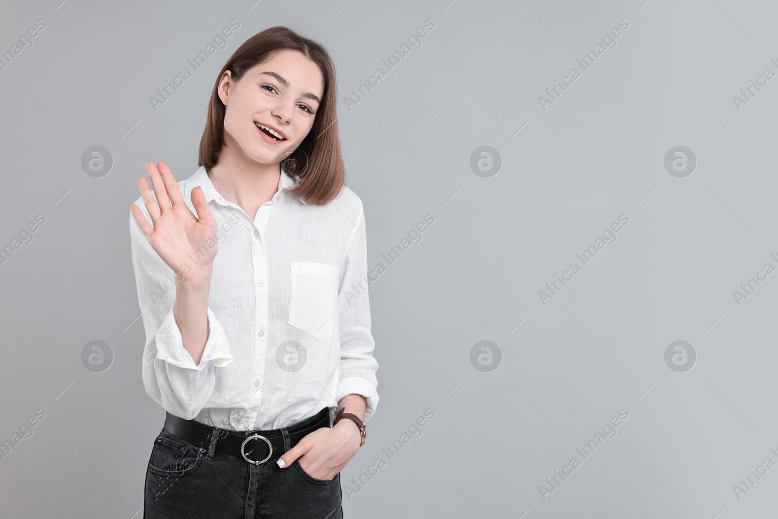 Photo of Happy teenage girl waving on gray background, space for text