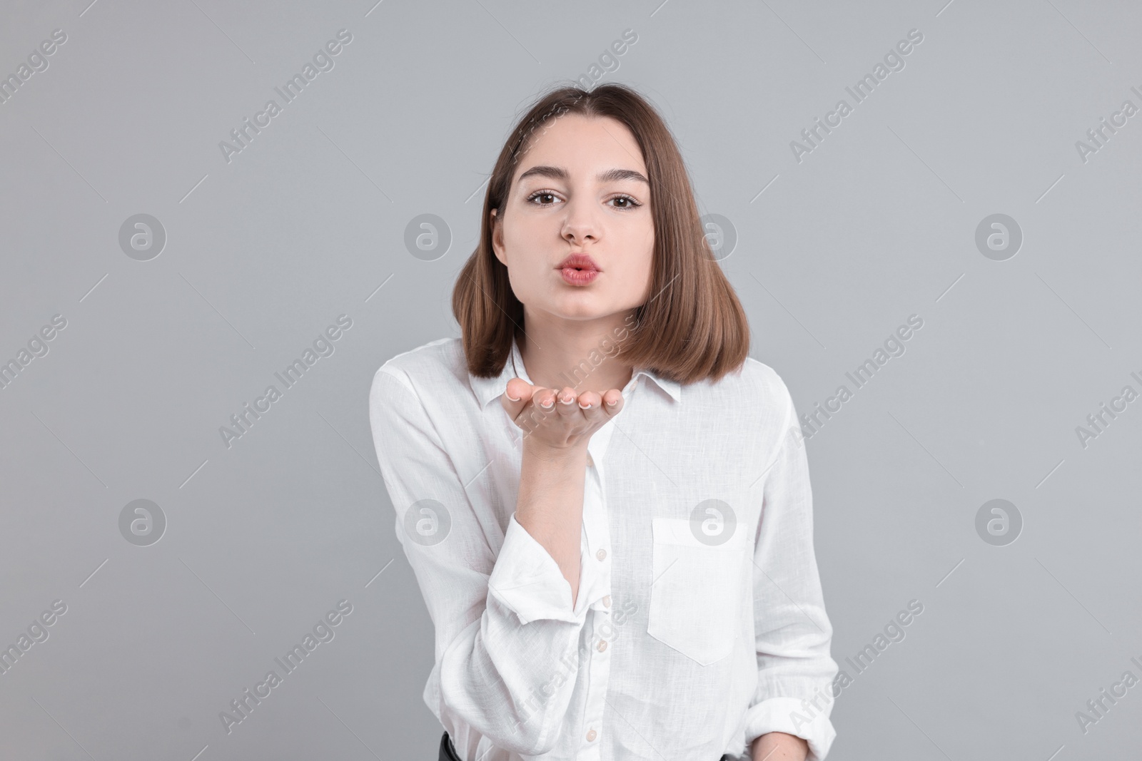 Photo of Beautiful teenage girl blowing kiss on gray background