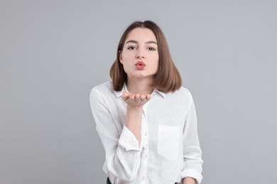 Beautiful teenage girl blowing kiss on gray background