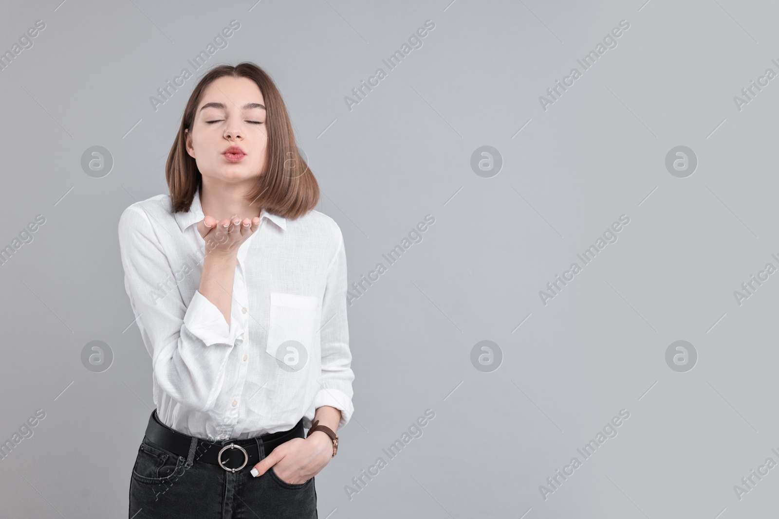 Photo of Beautiful teenage girl blowing kiss on gray background, space for text