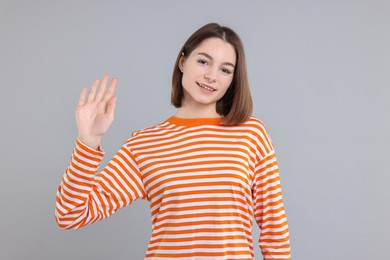 Happy teenage girl waving on gray background