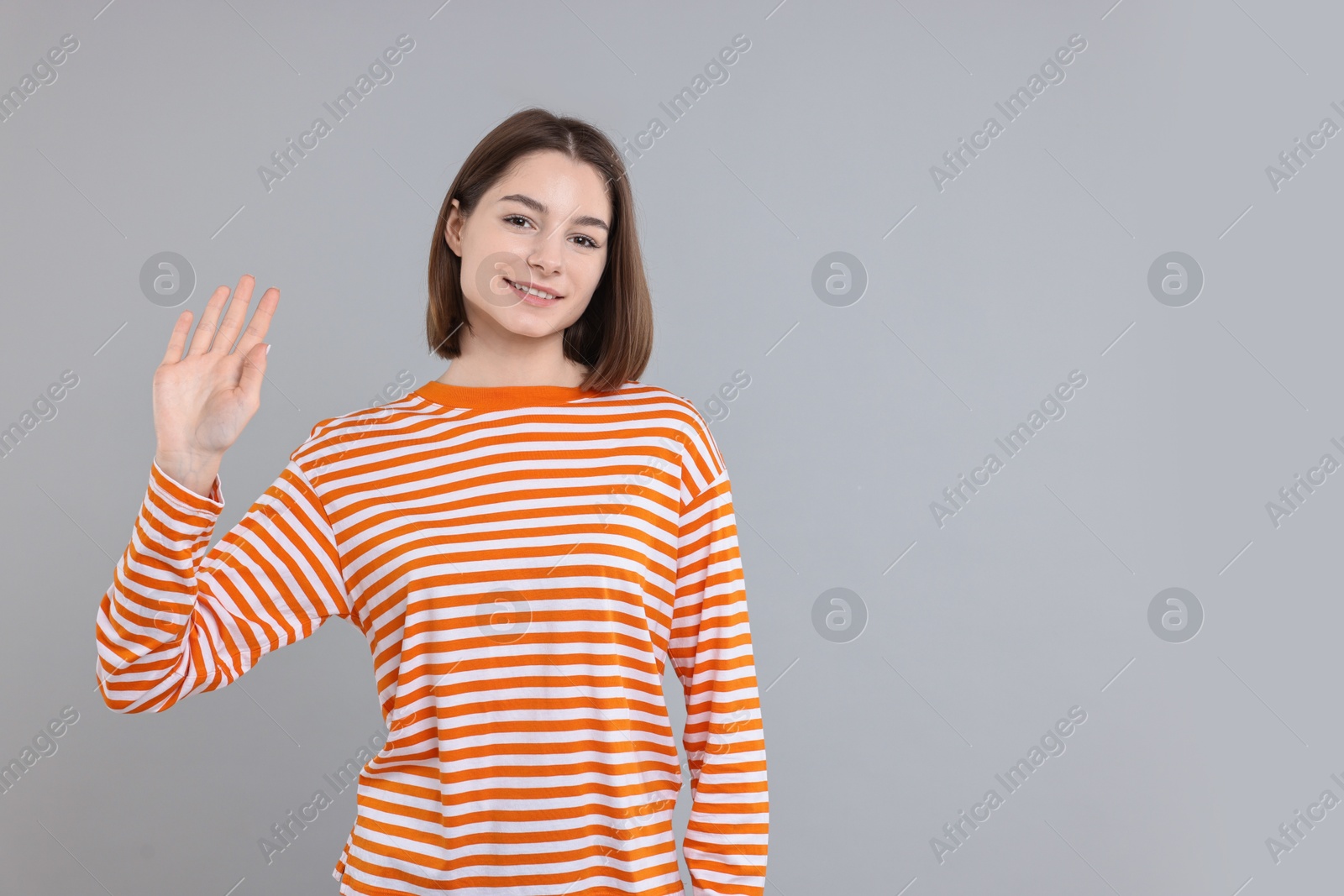 Photo of Happy teenage girl waving on gray background, space for text