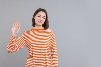 Photo of Happy teenage girl waving on gray background, space for text