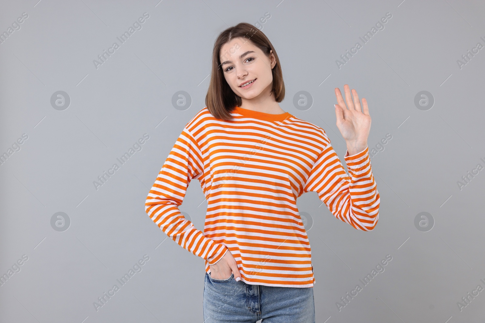 Photo of Happy teenage girl waving on gray background