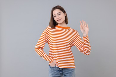 Happy teenage girl waving on gray background