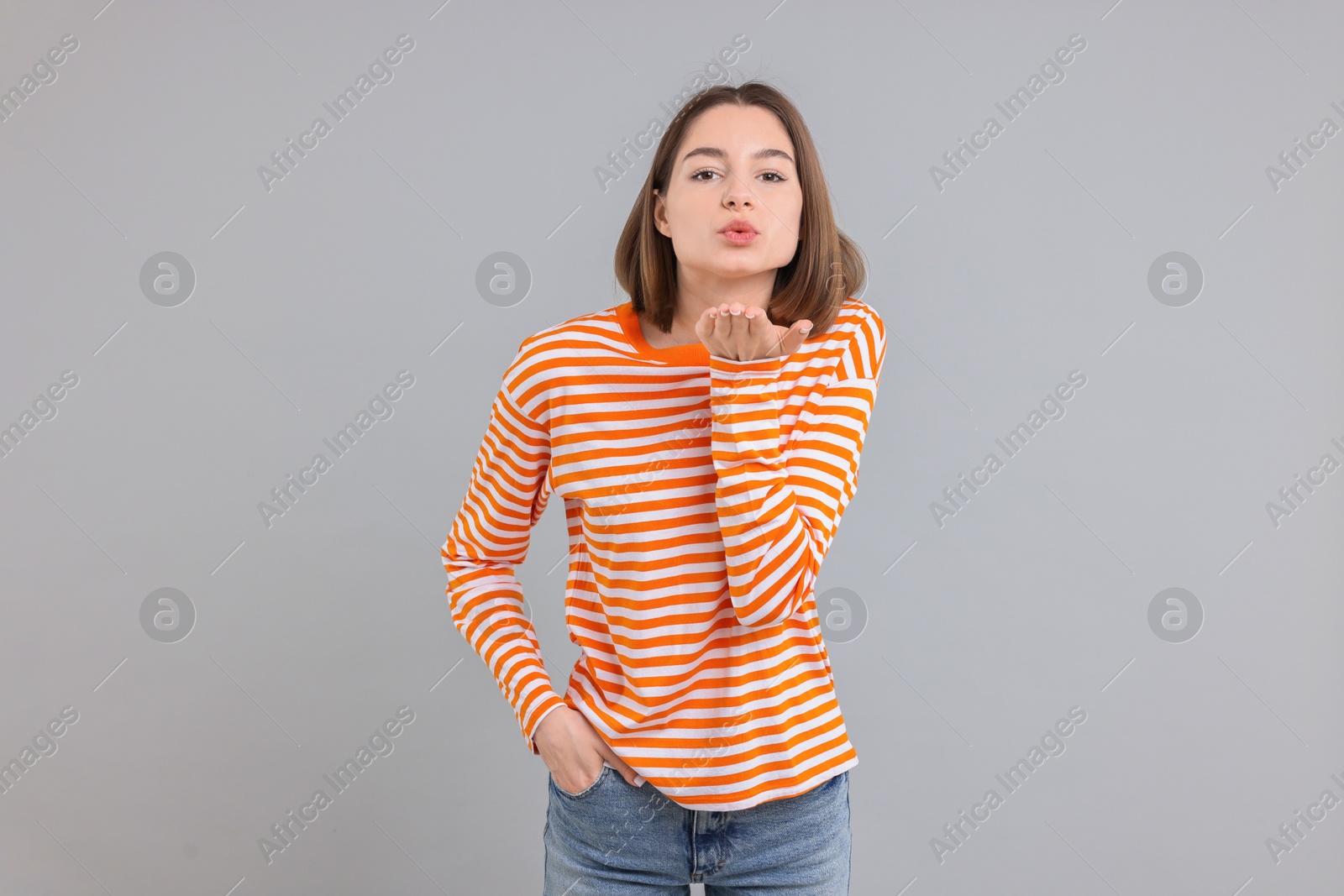 Photo of Beautiful teenage girl blowing kiss on gray background