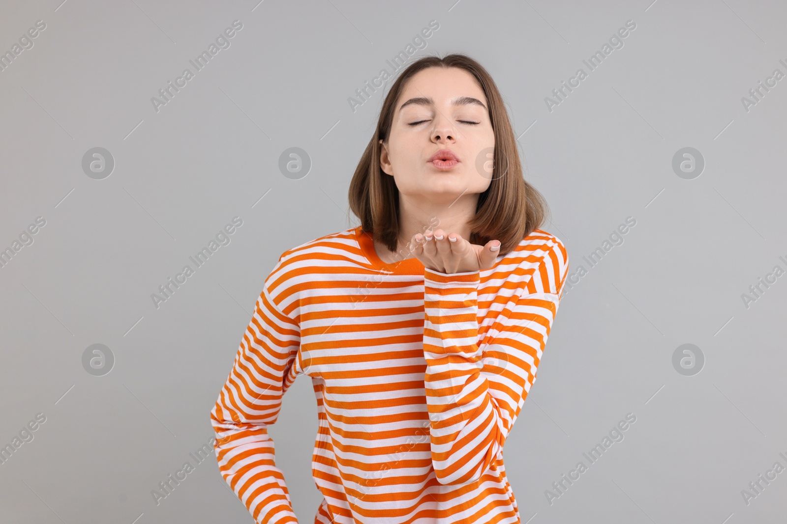 Photo of Beautiful teenage girl blowing kiss on gray background