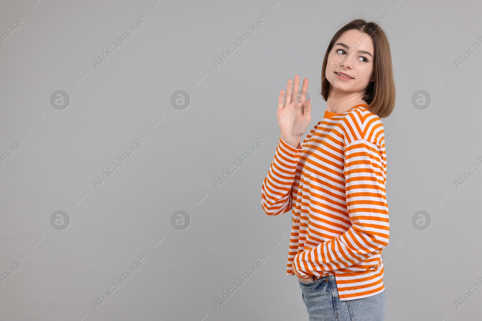 Photo of Happy teenage girl waving on gray background, space for text