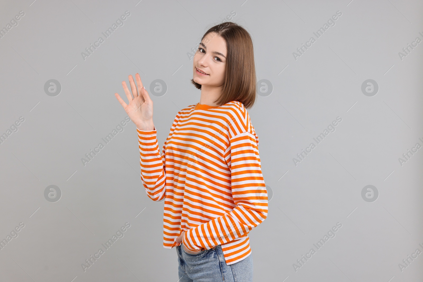 Photo of Happy teenage girl waving on gray background