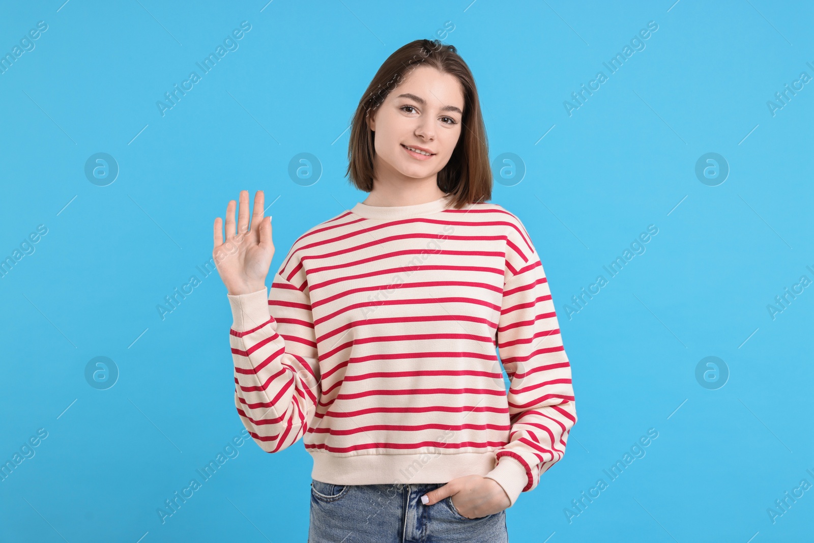 Photo of Happy teenage girl waving on light blue background