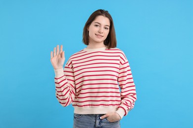 Happy teenage girl waving on light blue background