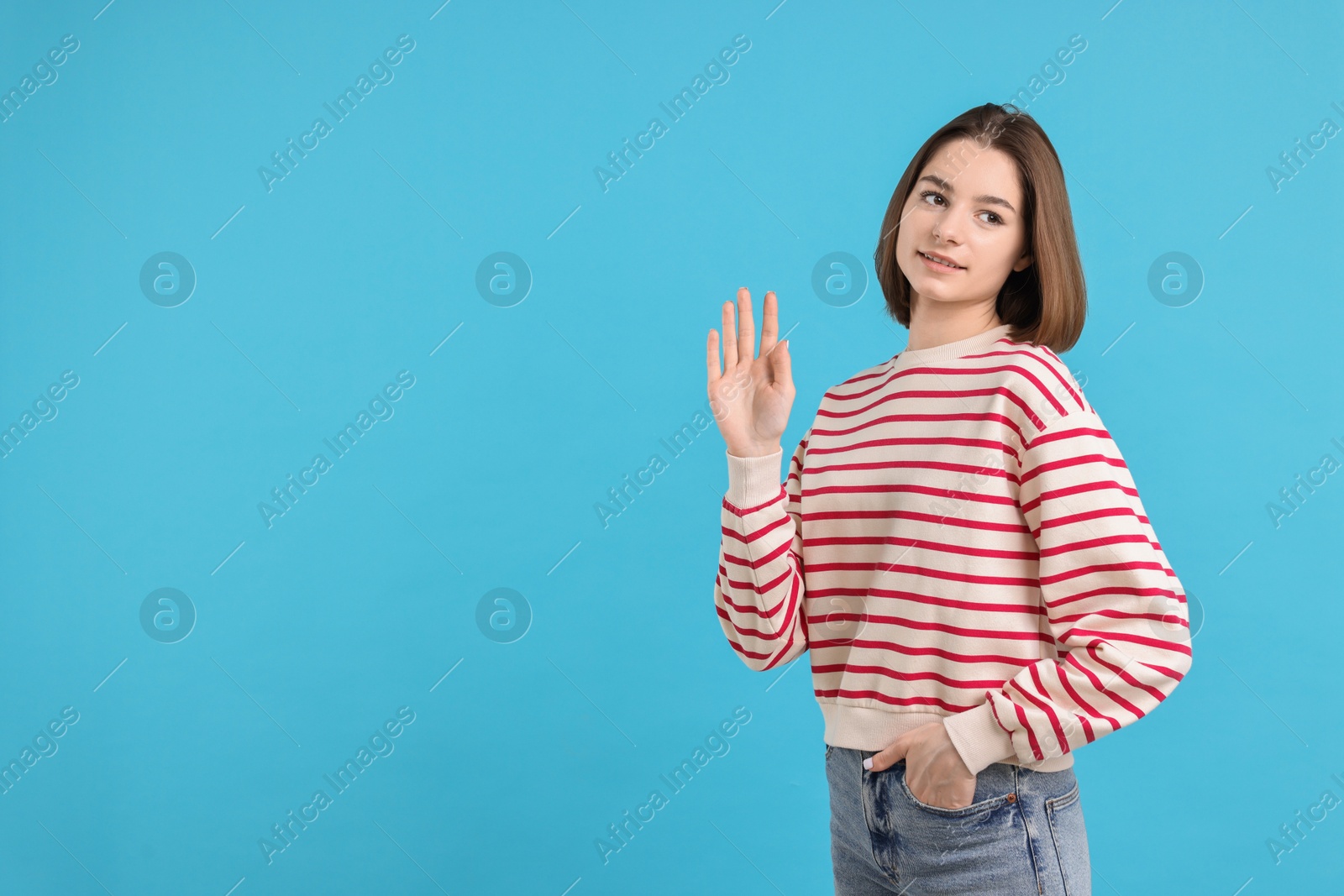 Photo of Happy teenage girl waving on light blue background, space for text