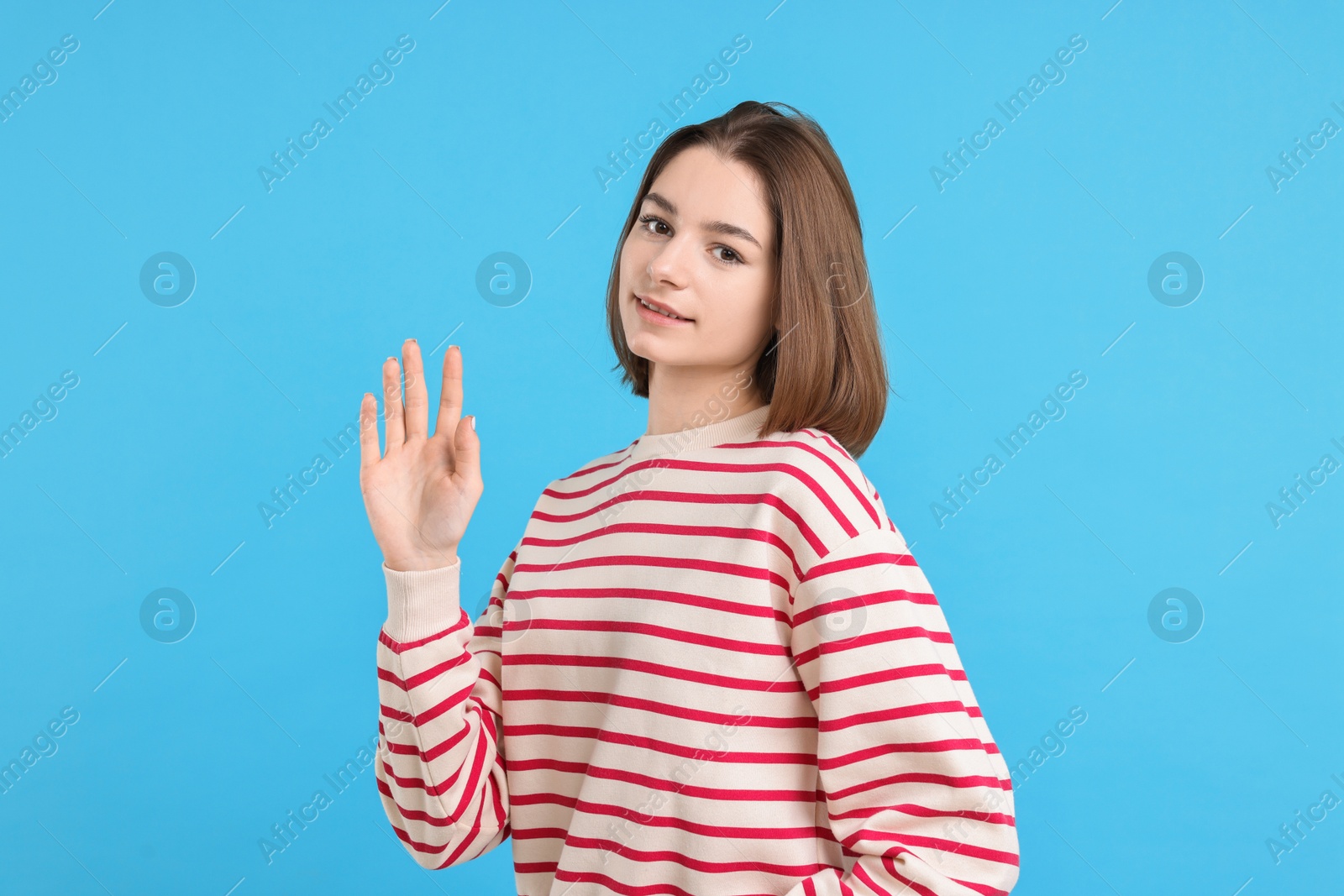 Photo of Beautiful teenage girl waving on light blue background