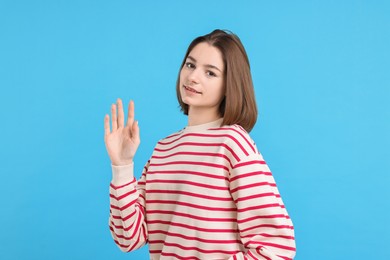 Photo of Beautiful teenage girl waving on light blue background