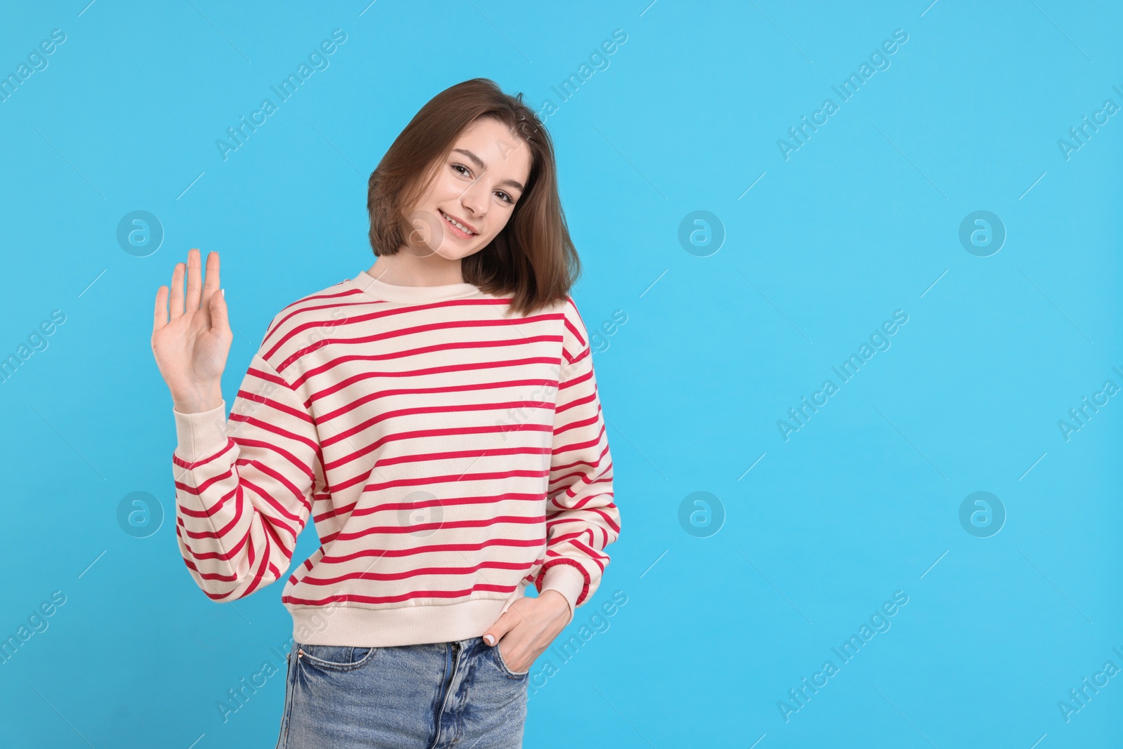 Photo of Happy teenage girl waving on light blue background, space for text