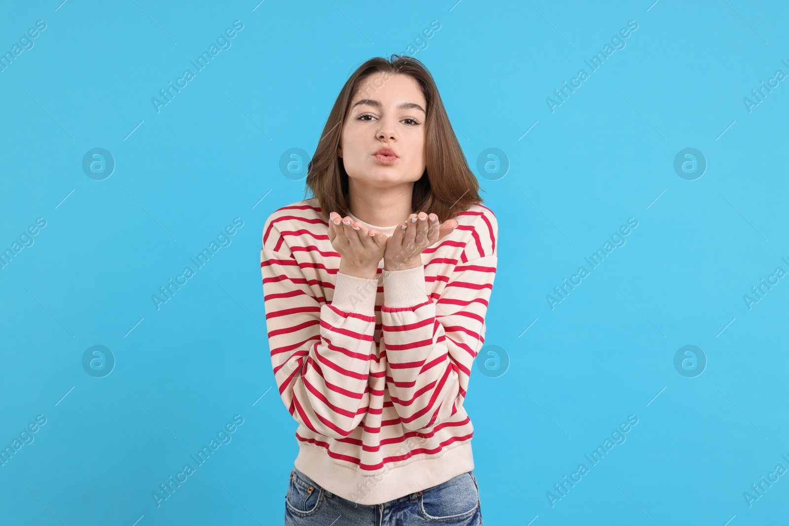 Photo of Beautiful teenage girl blowing kiss on light blue background