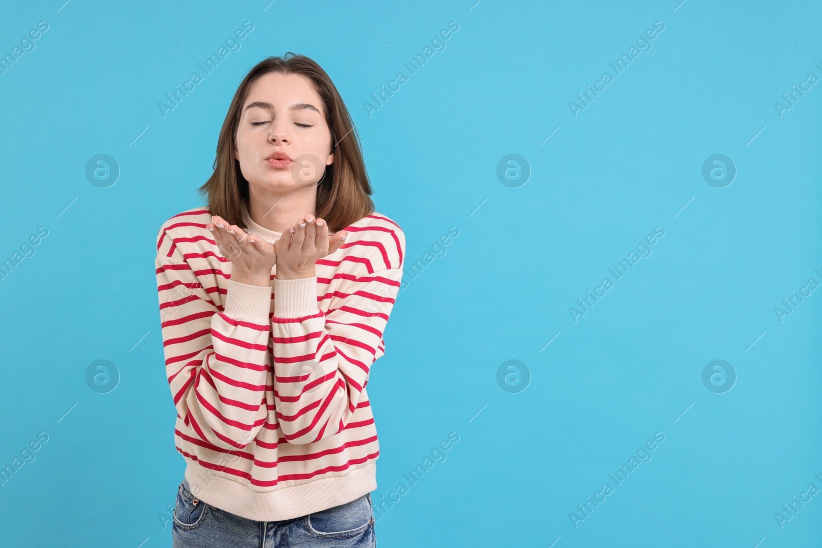 Photo of Beautiful teenage girl blowing kiss on light blue background, space for text