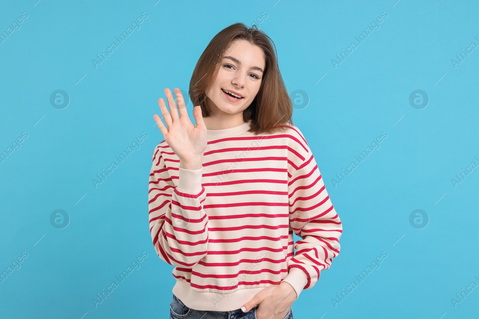 Photo of Happy teenage girl waving on light blue background