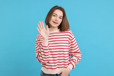 Happy teenage girl waving on light blue background