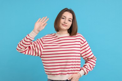 Photo of Beautiful teenage girl waving on light blue background