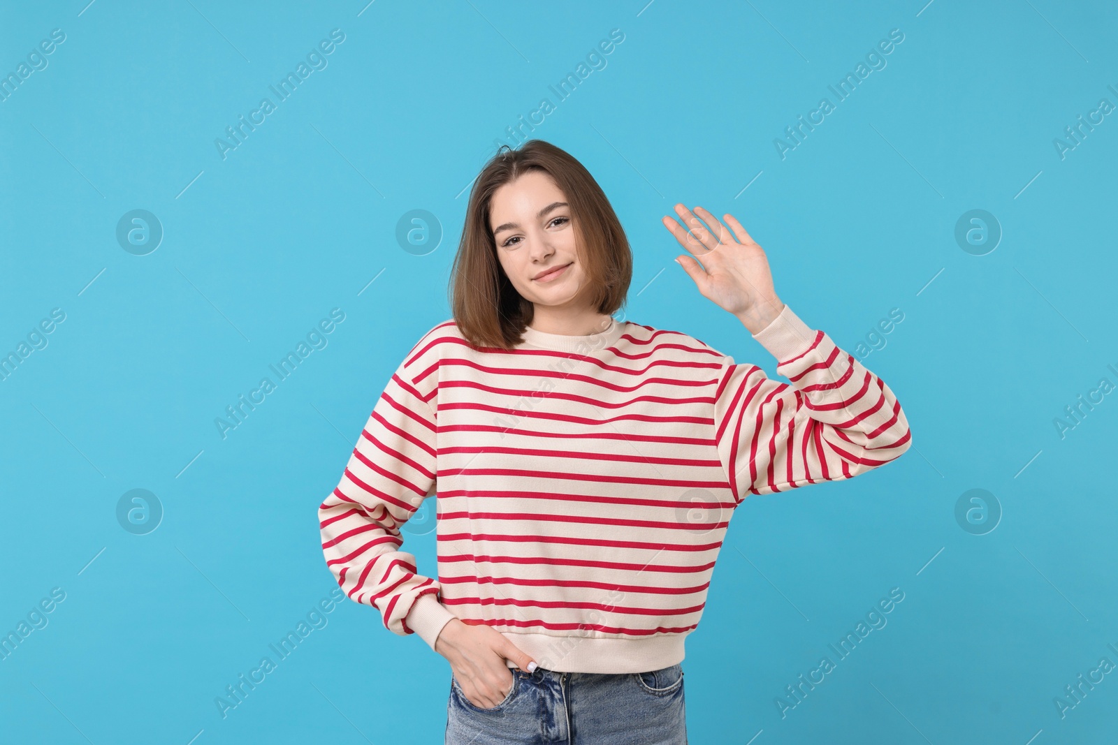 Photo of Beautiful teenage girl waving on light blue background