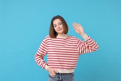 Beautiful teenage girl waving on light blue background