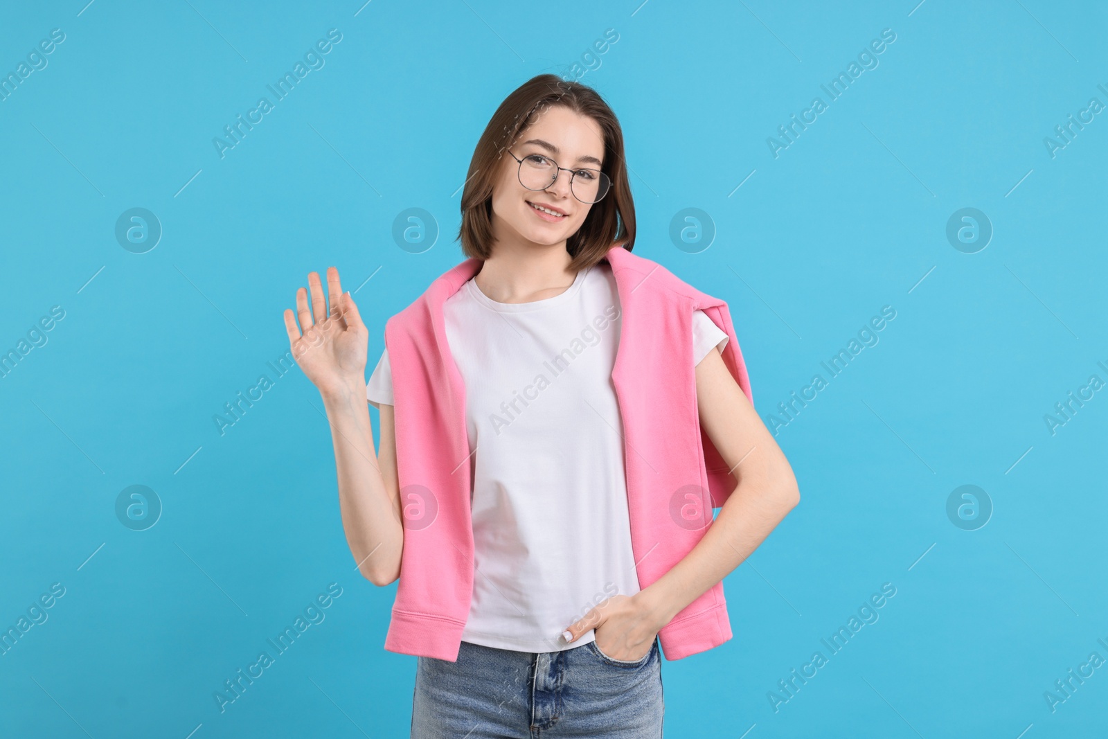 Photo of Happy teenage girl waving on light blue background