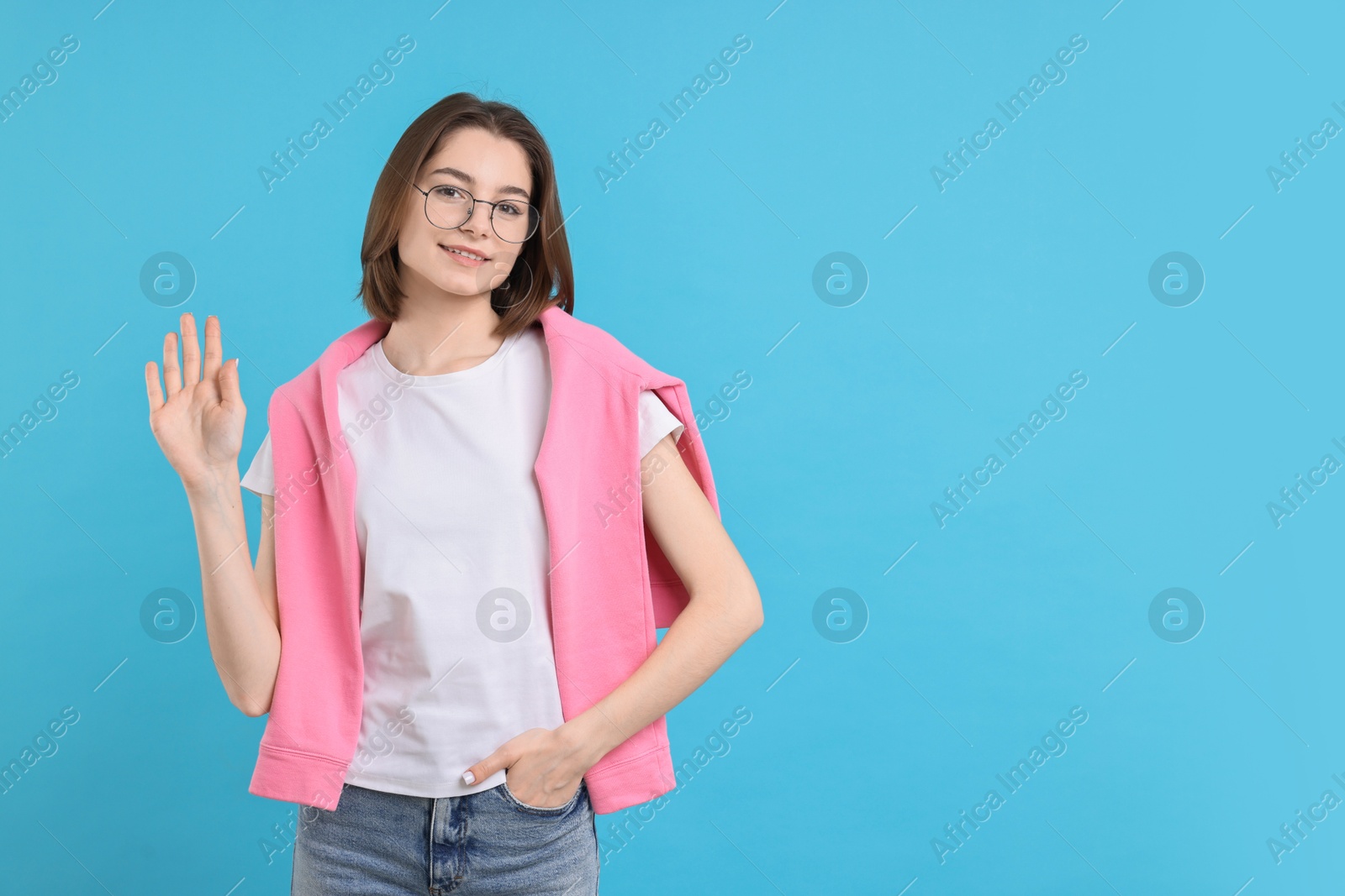 Photo of Happy teenage girl waving on light blue background, space for text