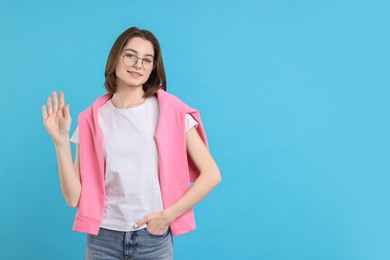 Photo of Happy teenage girl waving on light blue background, space for text