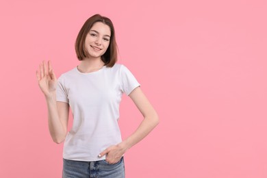 Photo of Happy teenage girl waving on pink background, space for text