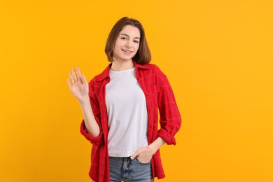 Photo of Happy teenage girl waving on orange background