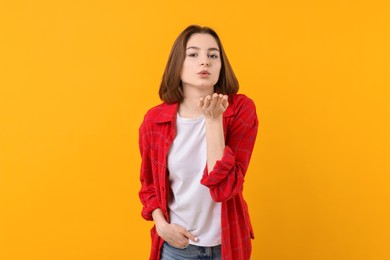 Photo of Beautiful teenage girl blowing kiss on orange background