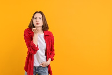 Photo of Beautiful teenage girl blowing kiss on orange background, space for text