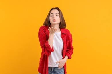 Photo of Beautiful teenage girl blowing kiss on orange background