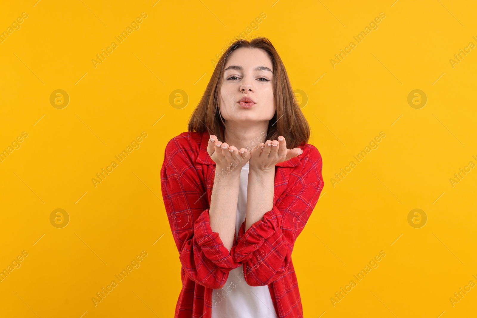 Photo of Beautiful teenage girl blowing kiss on orange background