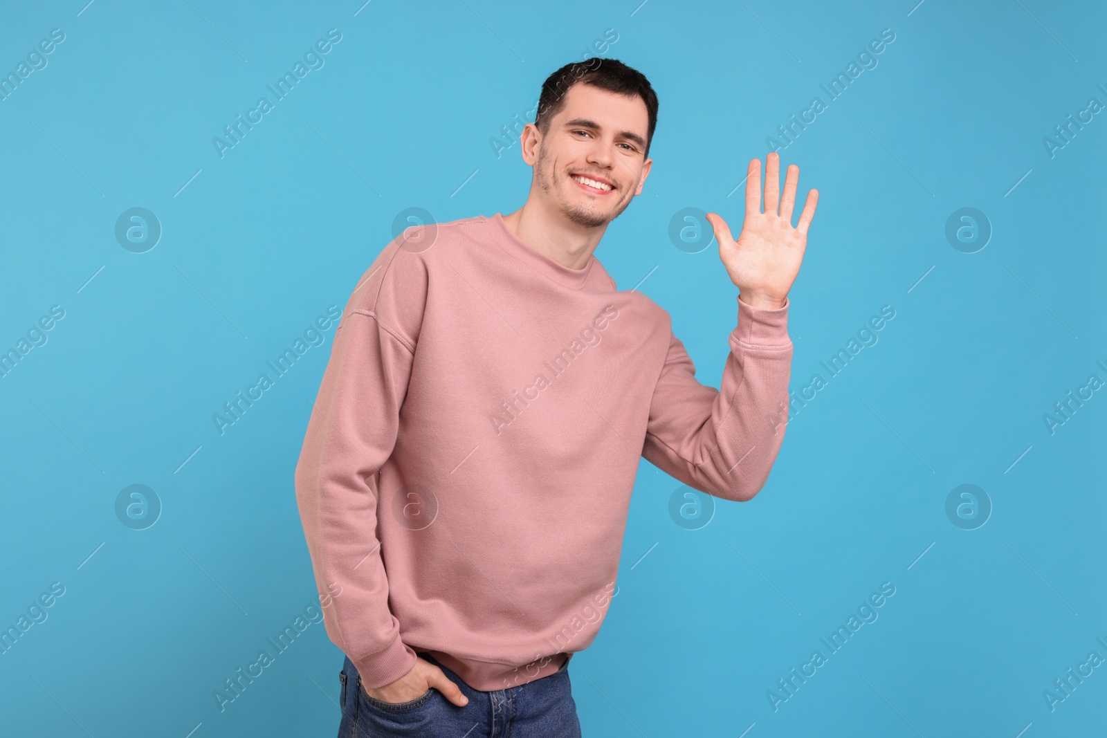 Photo of Happy young man waving on light blue background