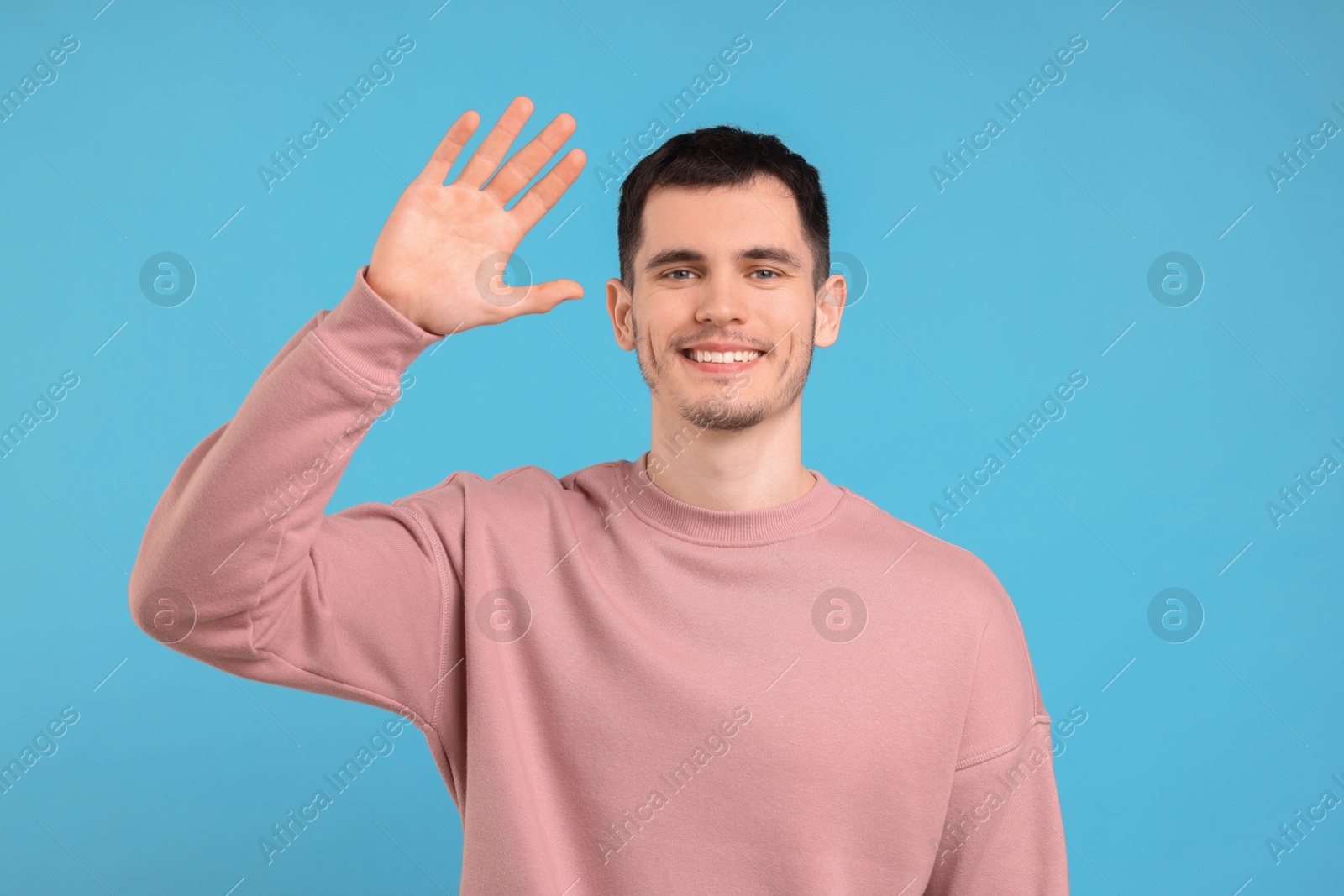 Photo of Happy young man waving on light blue background