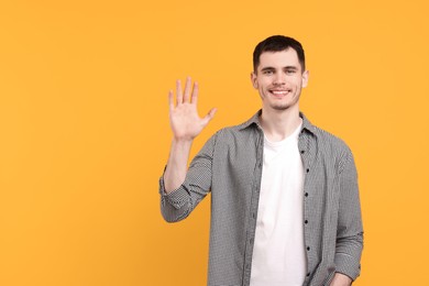 Photo of Happy young man waving on orange background