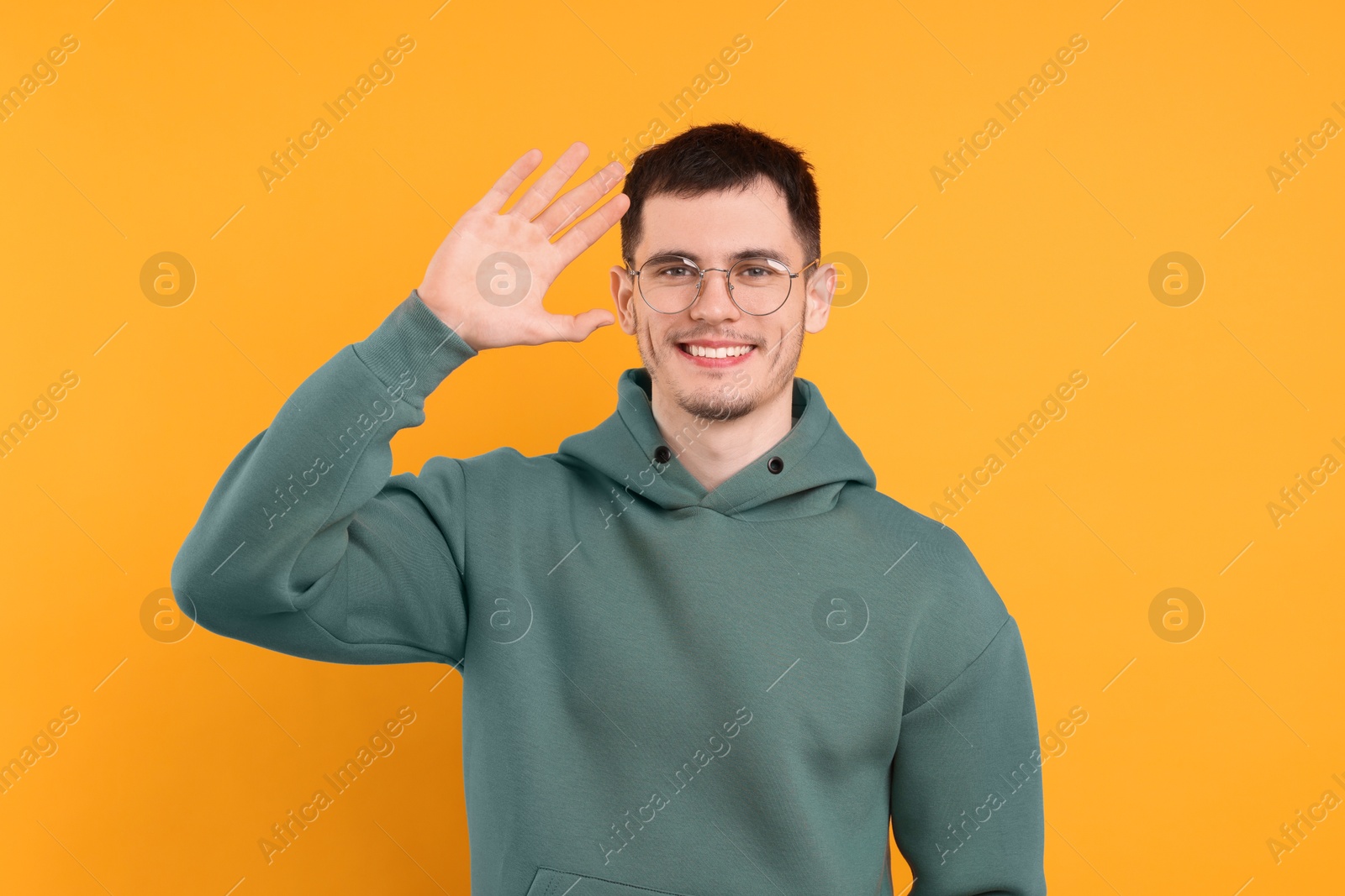 Photo of Happy young man waving on orange background