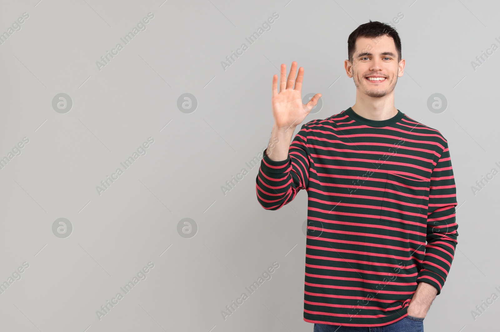 Photo of Happy young man waving on gray background, space for text