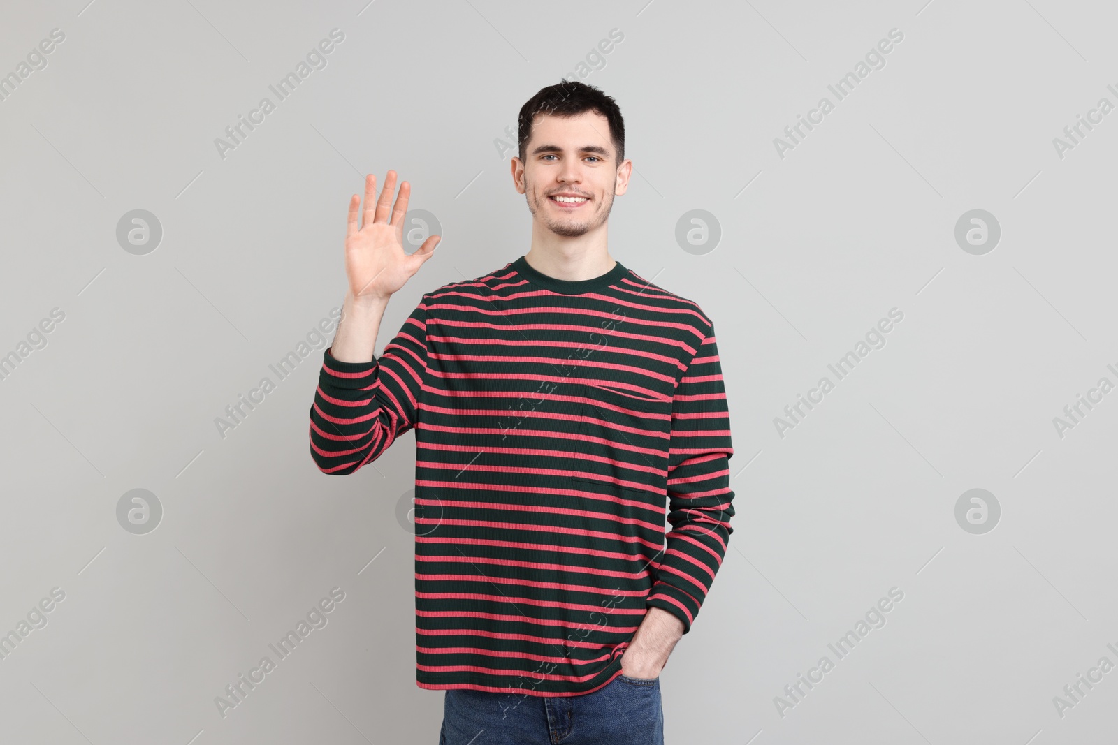 Photo of Happy young man waving on gray background