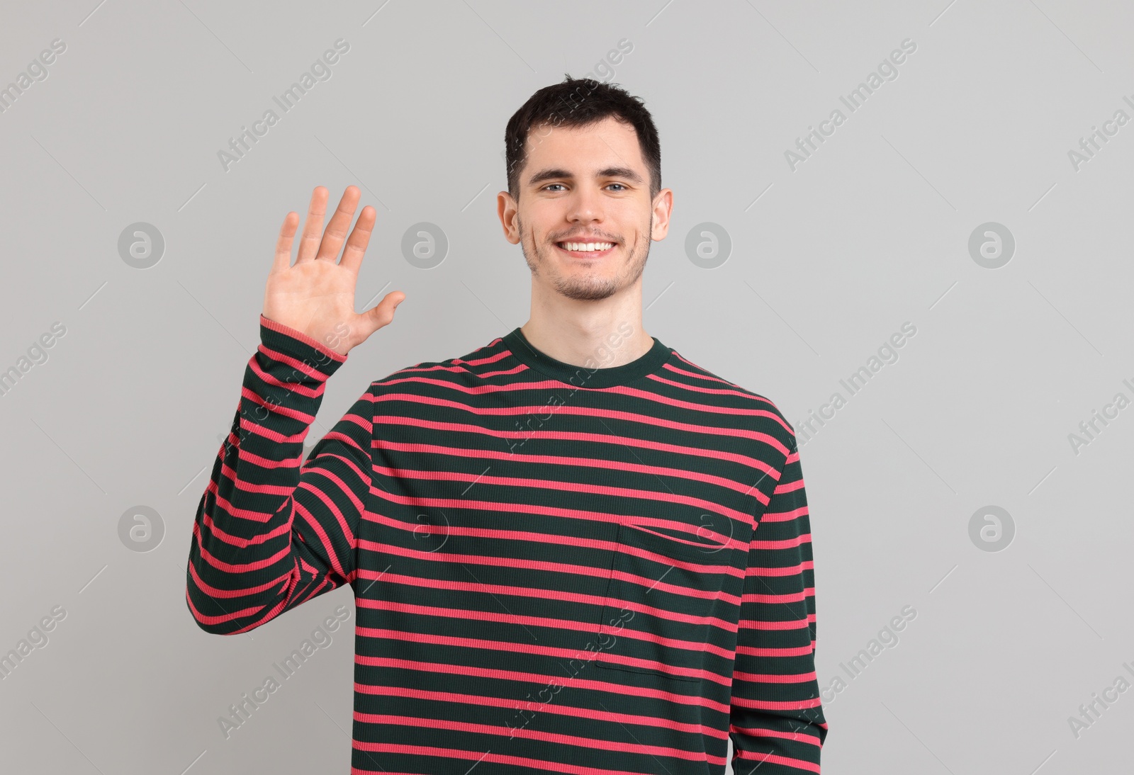 Photo of Happy young man waving on gray background