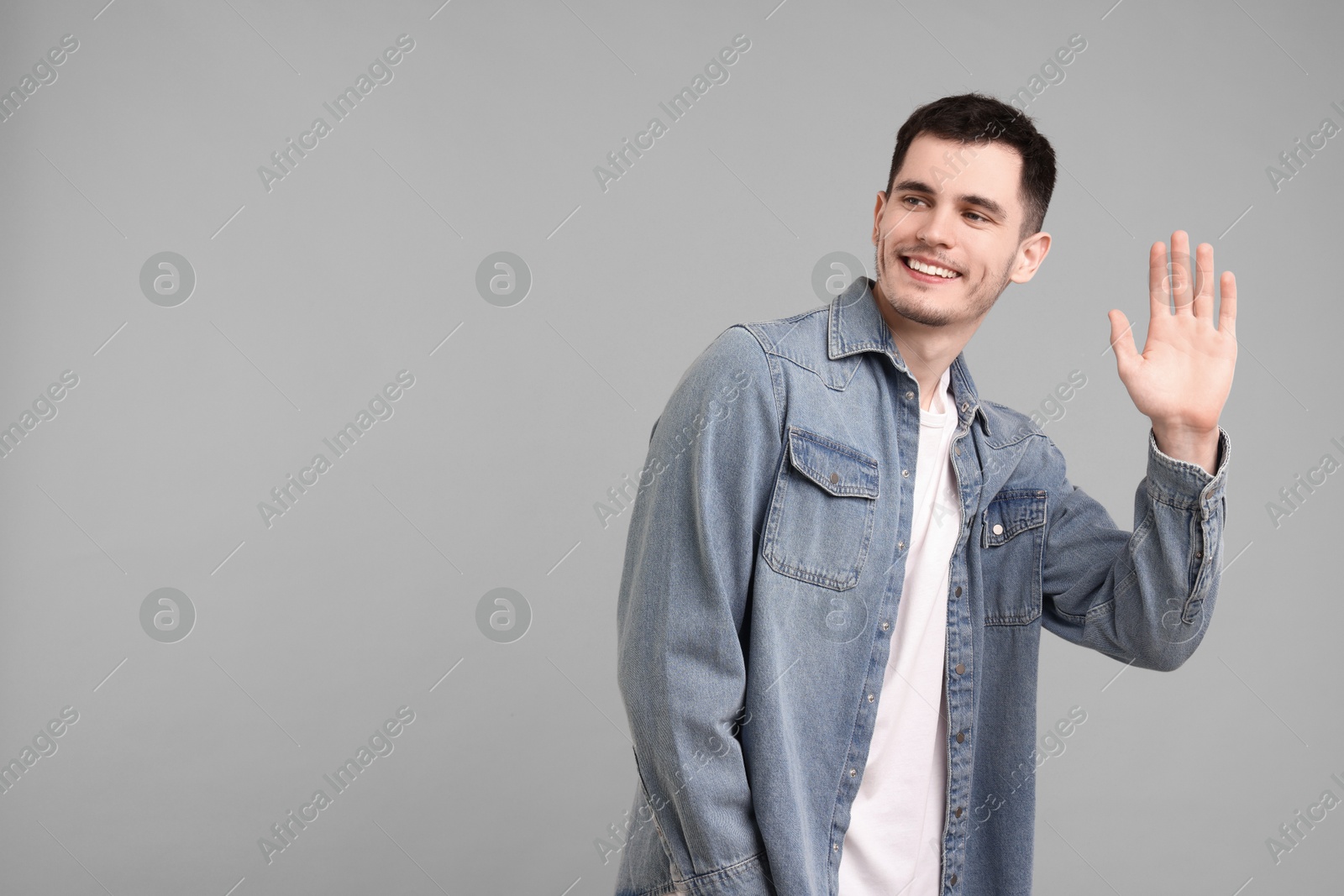 Photo of Happy young man waving on gray background, space for text