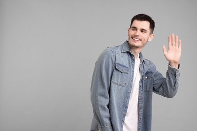 Happy young man waving on gray background, space for text