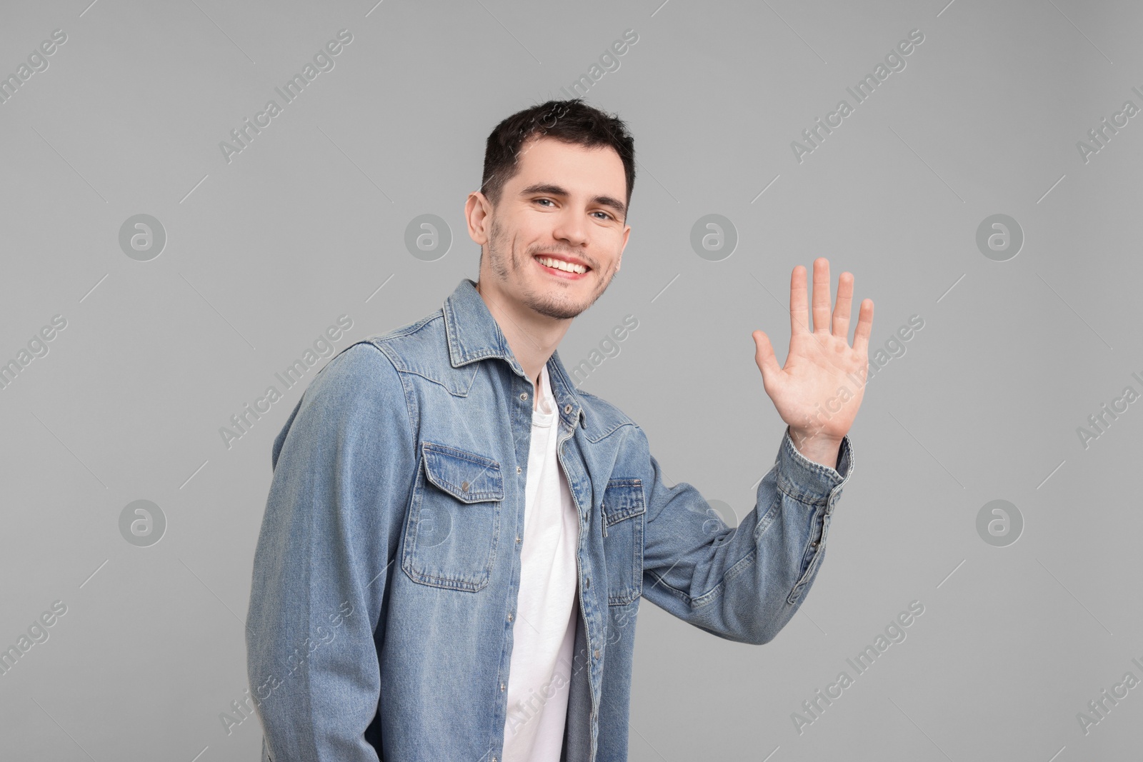 Photo of Happy young man waving on gray background